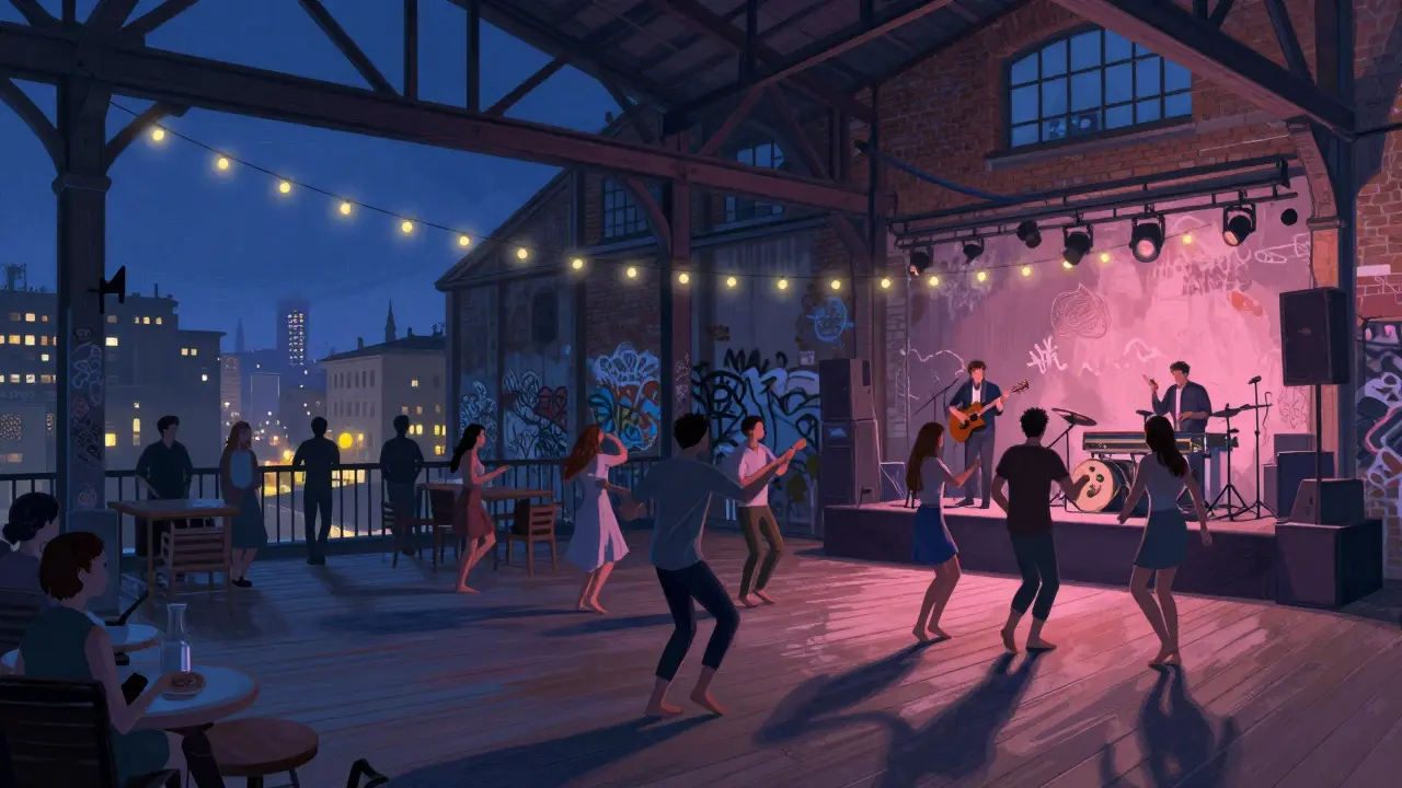 Young crowd dancing barefoot in a converted factory club with rooftop terrace and live music under string lights.